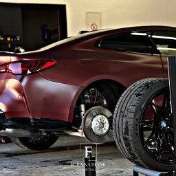 Fura na błysk - Bordowy, matowy BMW M4 po detailingu, z widocznymi tarczami hamulcowymi i czarną felgą na stojaku. W tle warsztat.