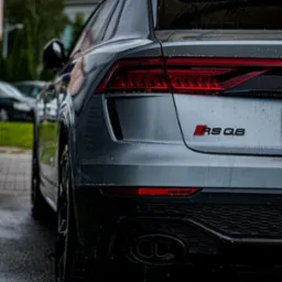 Szary samochód Audi RS Q8, widok z tyłu, mokry po umyciu, z widocznymi kroplami wody na karoserii i czarnym dyfuzorze z podwójnym wydechem.