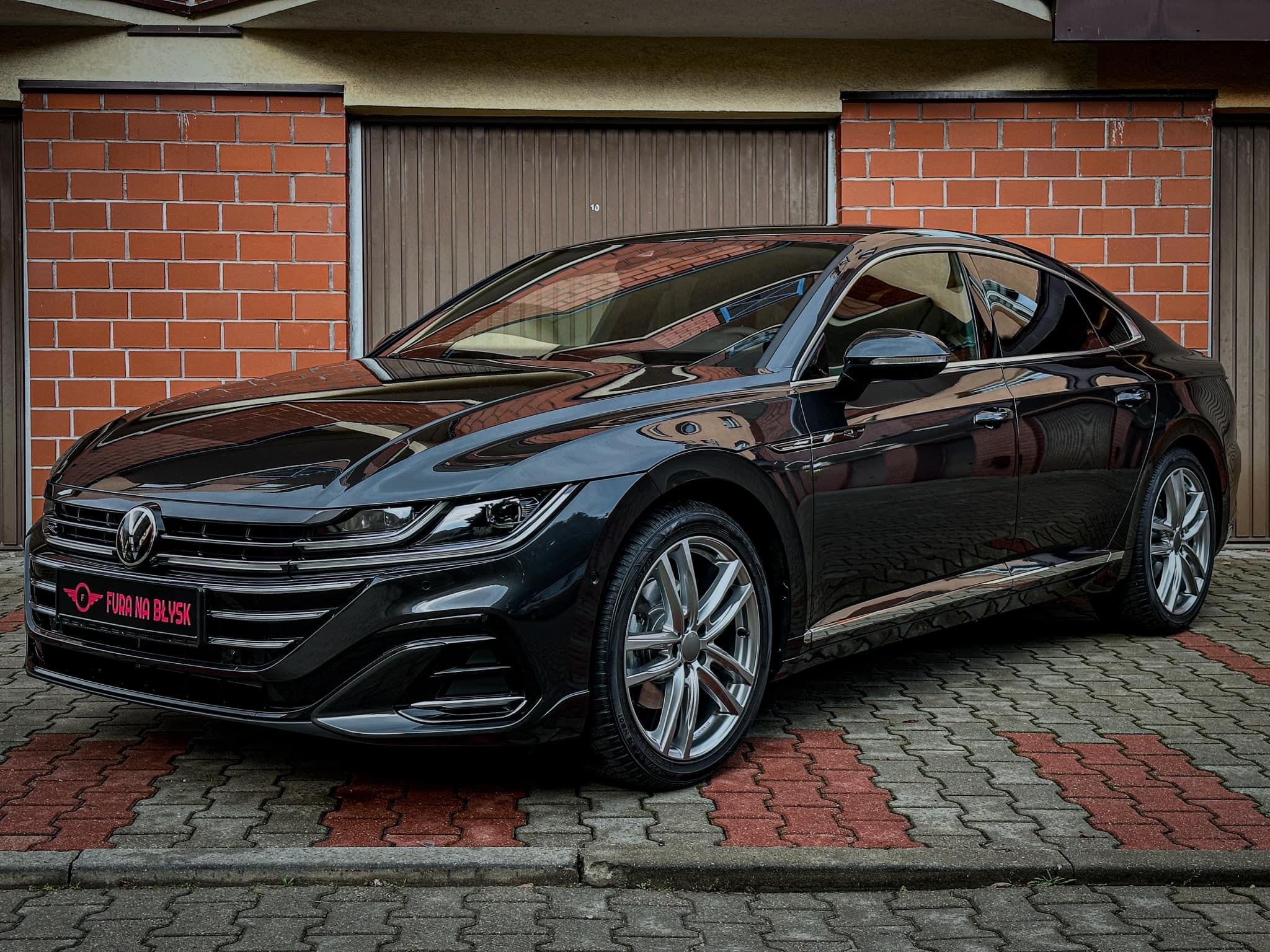 Błyszczący, czarny Volkswagen Arteon po kompleksowym myciu i detailingu, zaparkowany na kostce brukowej przed garażem z ceglaną ścianą.