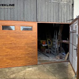 Vekline Agnieszka Markowska - Otwarta garażowa brama segmentowa w kolorze drewna, z dwoma małymi okienkami, zamontowana w budynku o szarej, drewnianej elewacji. Widoczne wnętrze garażu.
