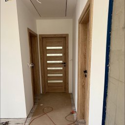 Vekline Agnieszka Markowska - Wnętrze korytarza z trzema zamontowanymi drzwiami wewnętrznymi o drewnianym wykończeniu, widoczne narzędzia i materiały budowlane.