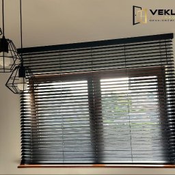 Vekline Agnieszka Markowska - Ciemne, drewniane żaluzje poziome zamontowane w oknie z drewnianą ramą. W tle widoczne światło dzienne. U góry zwisają trzy czarne lampy w stylu loft.