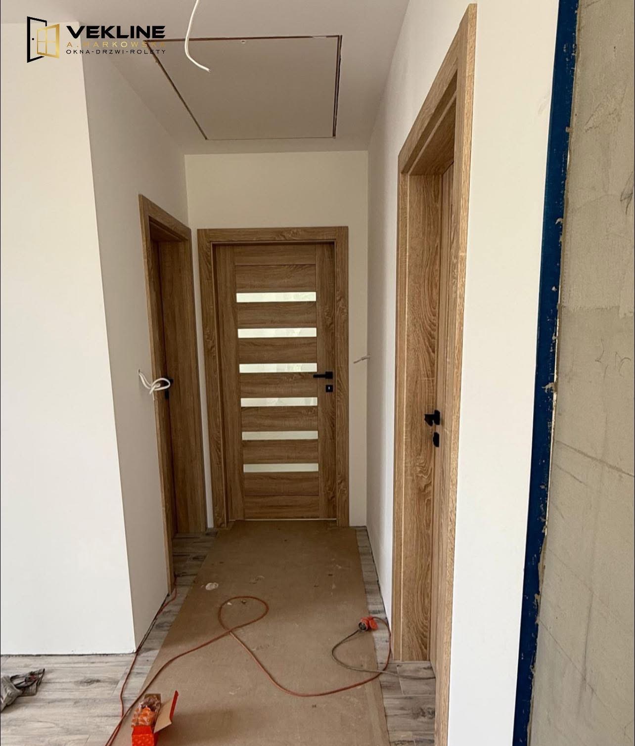 Wnętrze korytarza z trzema zamontowanymi drzwiami wewnętrznymi o drewnianym wykończeniu, widoczne narzędzia i materiały budowlane.