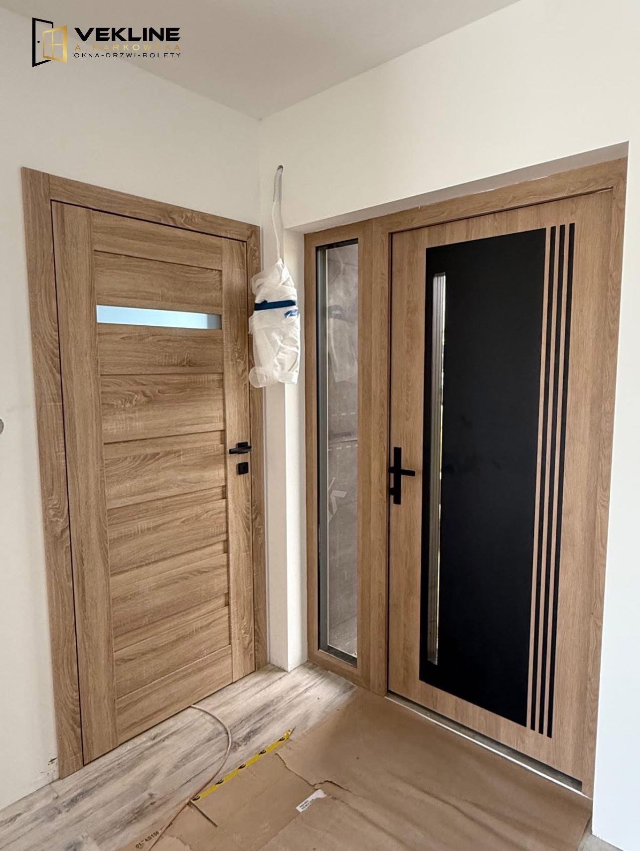 Dwa różne modele drzwi wewnętrznych w odcieniach drewna, z czarnymi akcentami i przeszkleniami, zamontowane w narożniku pomieszczenia w trakcie prac wykończeniowych.