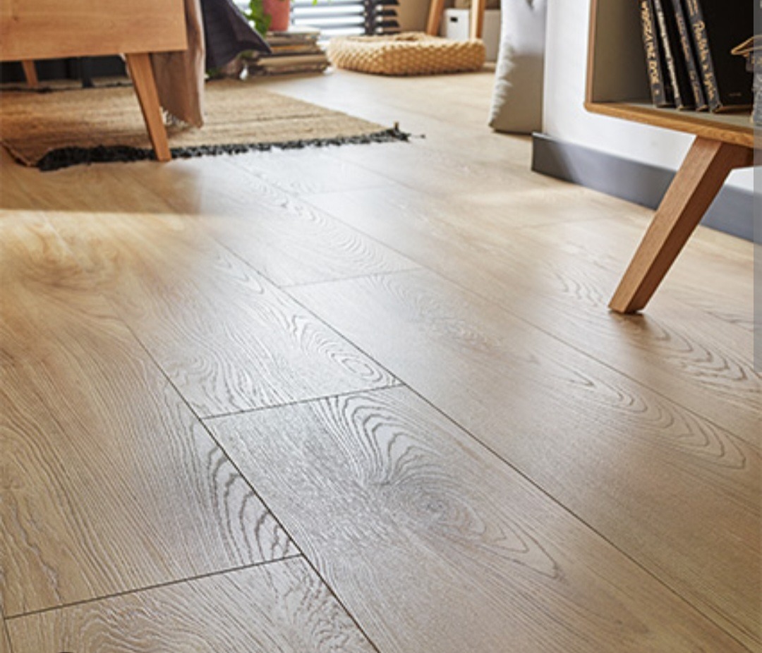 Jasne panele podłogowe z widoczną strukturą drewna, ułożone w salonie z elementami wystroju w tle.