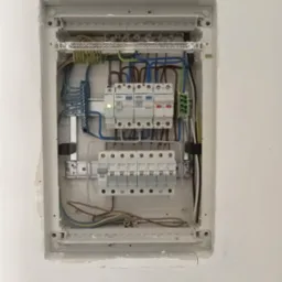 Rozdzielnica elektryczna z zainstalowanymi bezpiecznikami i okablowaniem, widoczne ślady po montażu w ścianie.