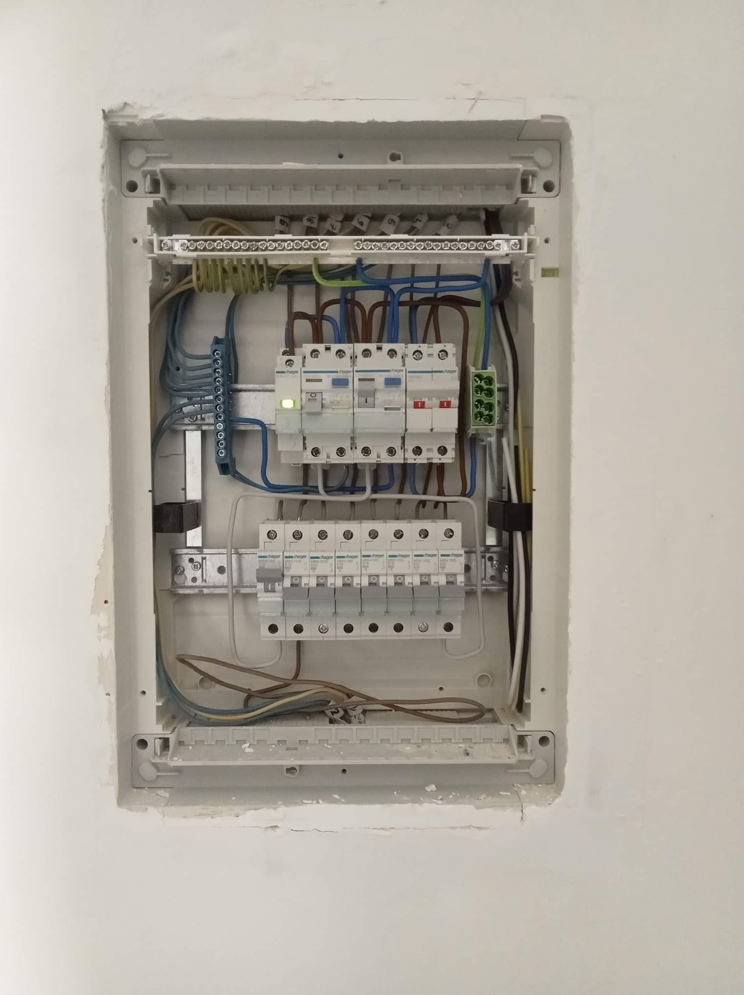 Rozdzielnica elektryczna z zainstalowanymi bezpiecznikami i okablowaniem, widoczne ślady po montażu w ścianie.