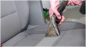 Czyszczenie jasnoszarego fotela samochodowego przy użyciu profesjonalnego odkurzacza ekstrakcyjnego z przezroczystą dyszą trójkątną, w rękawicach ochronnych.