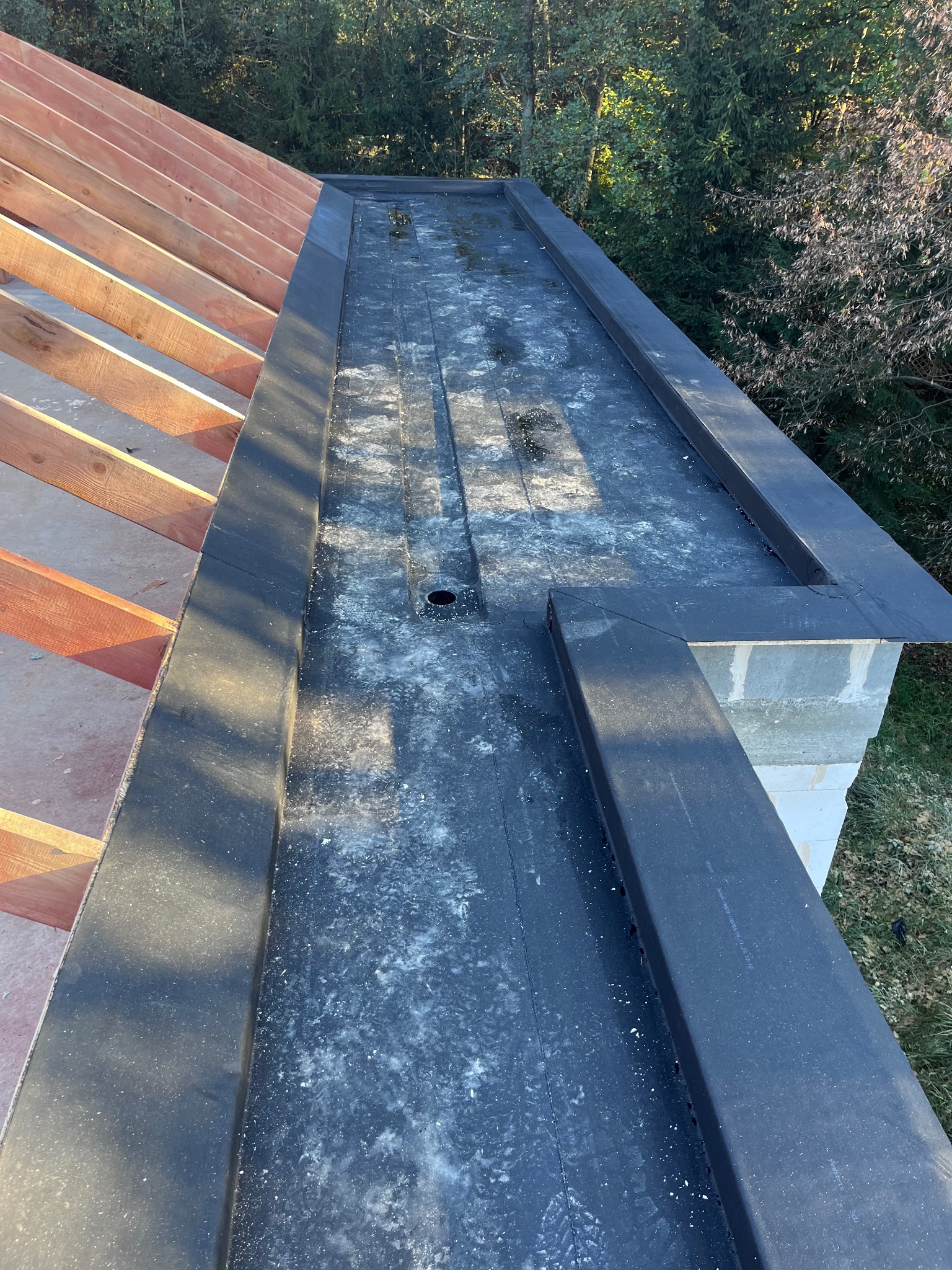 Fragment dachu płaskiego z konstrukcją drewnianą i obróbkami blacharskimi, widoczne ślady zabrudzeń na powierzchni papy.