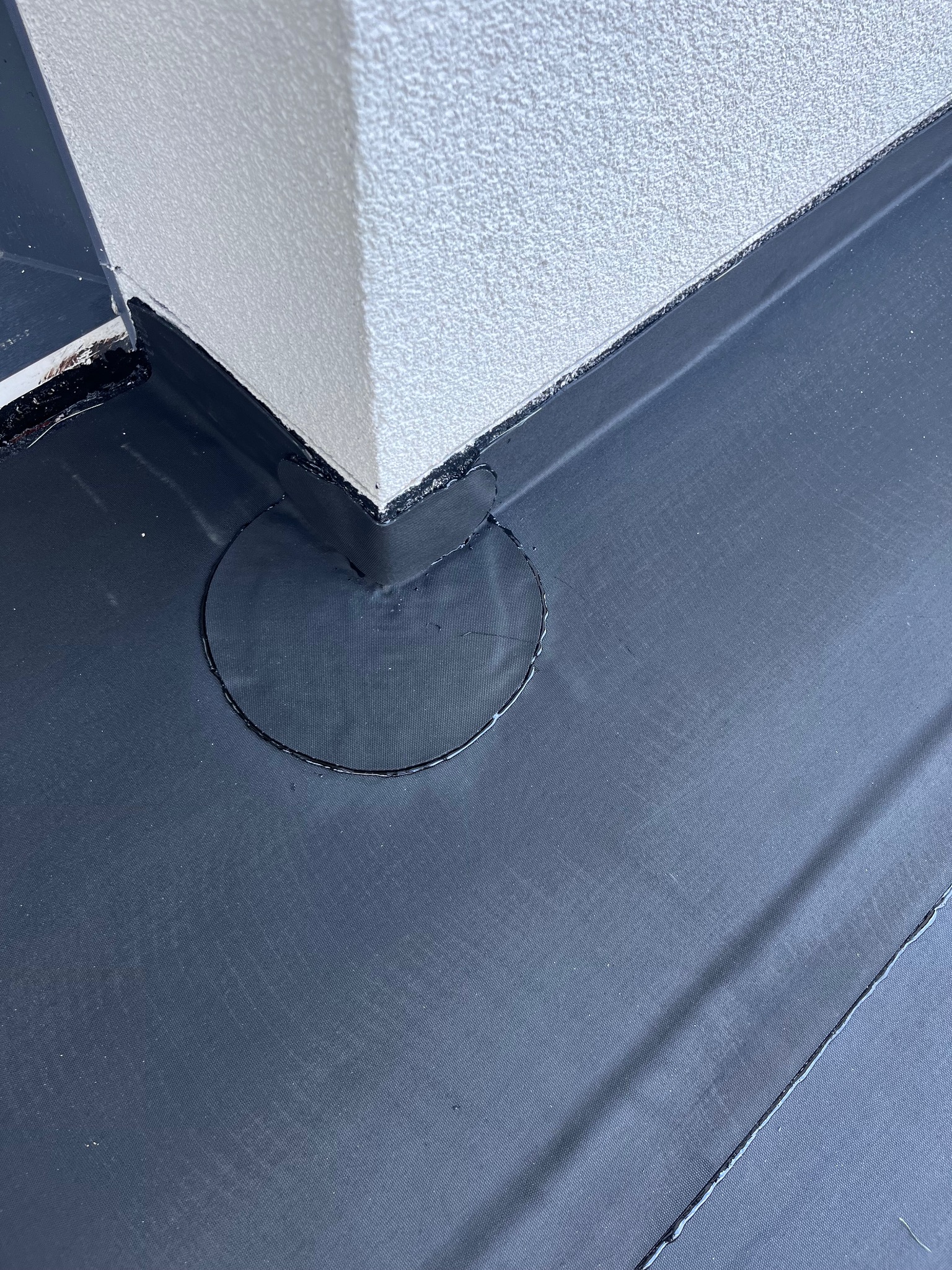 Szczelne, czarne pokrycie dachowe z widocznym okrągłym odpływem przy krawędzi ściany budynku.