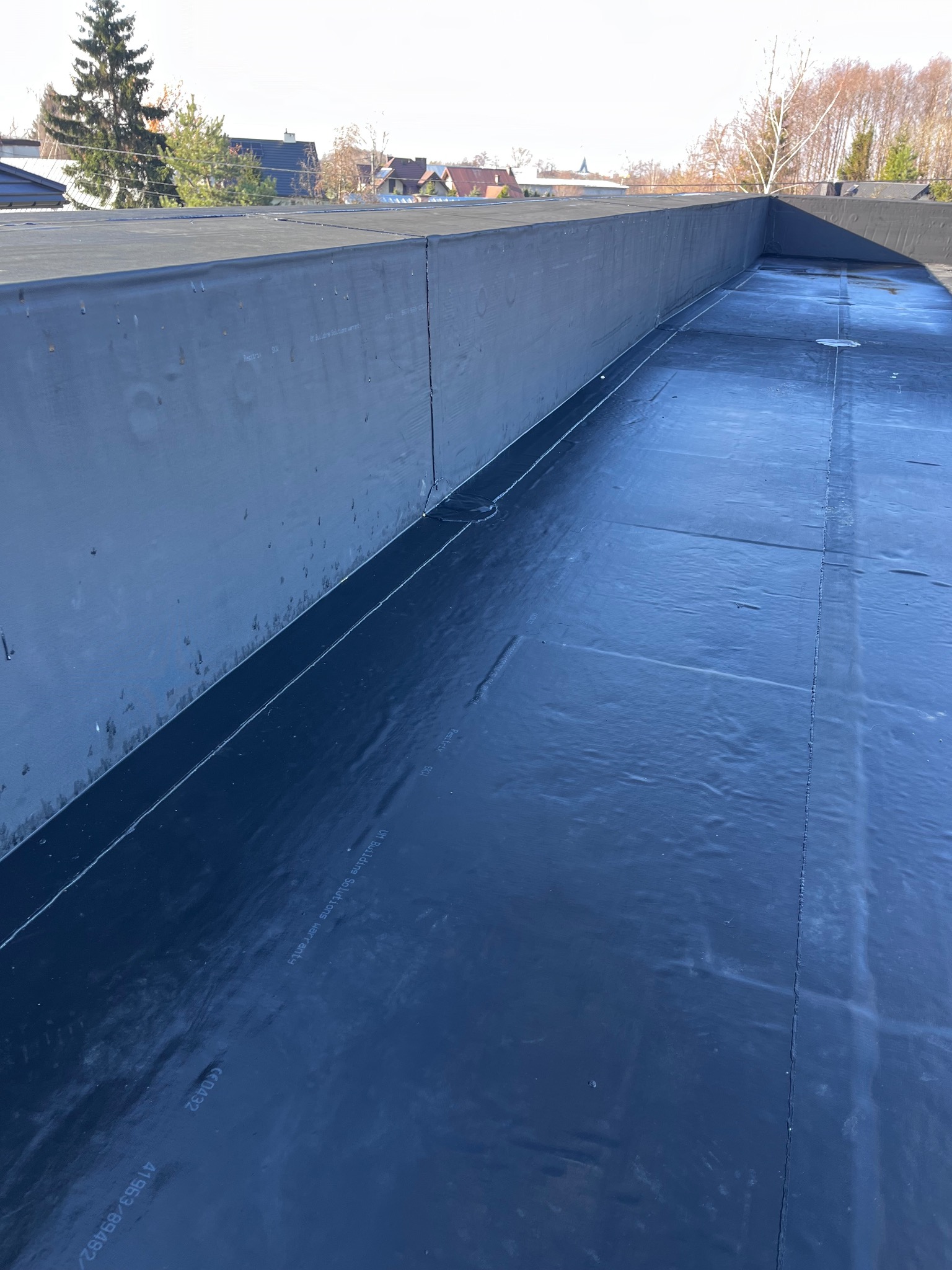 Nowe, czarne pokrycie dachowe z papy na płaskim dachu budynku, widoczne łączenia i tekstury materiału.