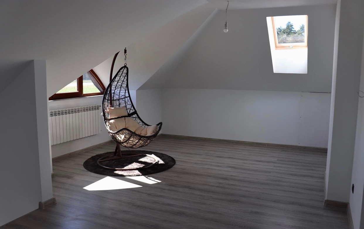 Poddasze po remoncie z drewnianą podłogą, wiszącym fotelem kokonem i oknem dachowym wpuszczającym jasne światło.