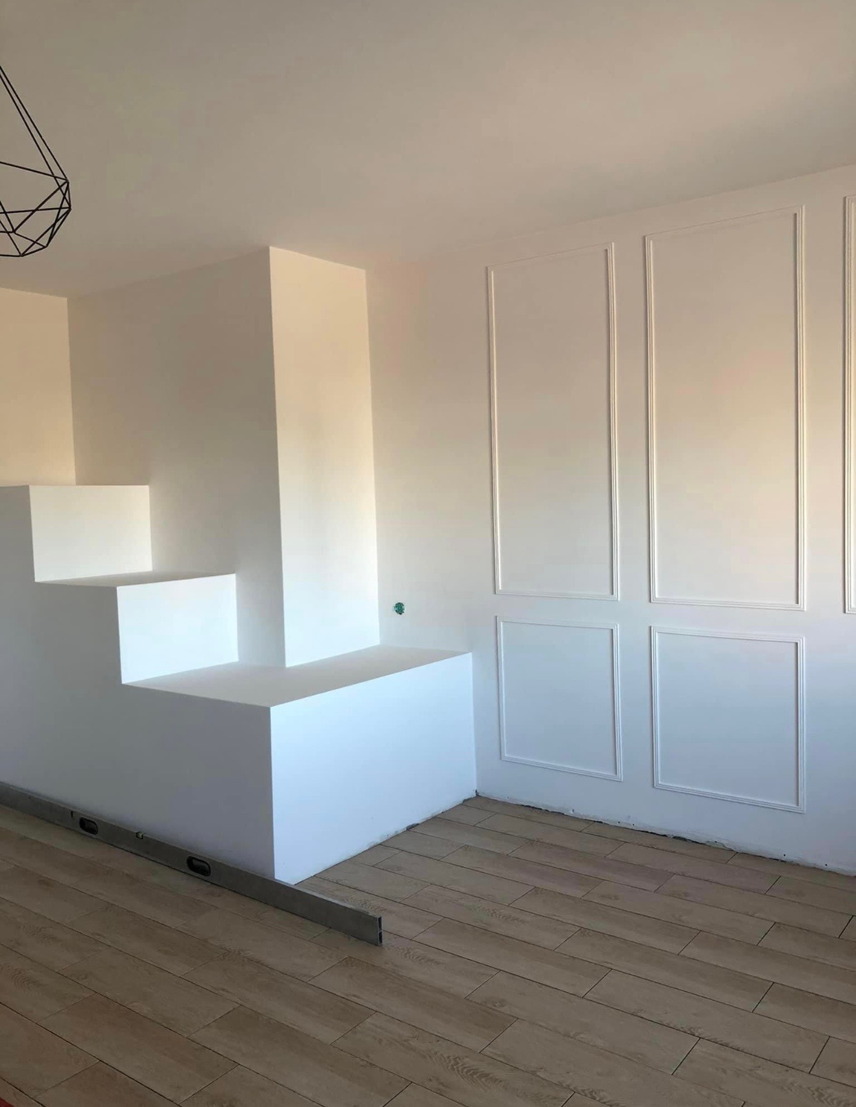 Białe, geometryczne schody w nowoczesnym wnętrzu z panelami ściennymi, poziomica na podłodze.