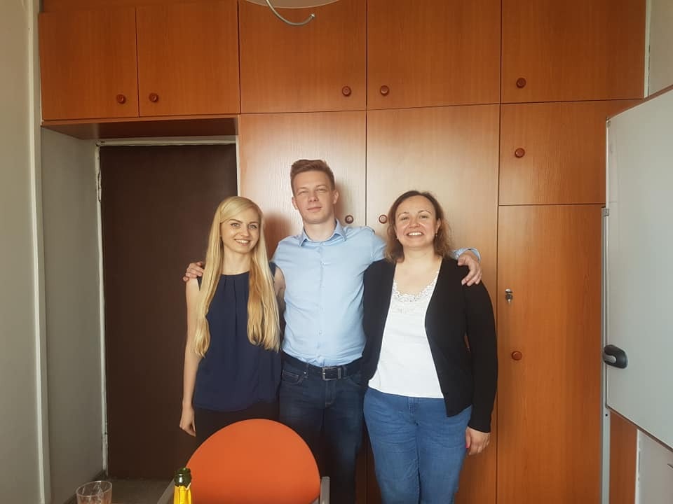 Trzy osoby uśmiechnięte stojące w biurze na tle drewnianych szafek.