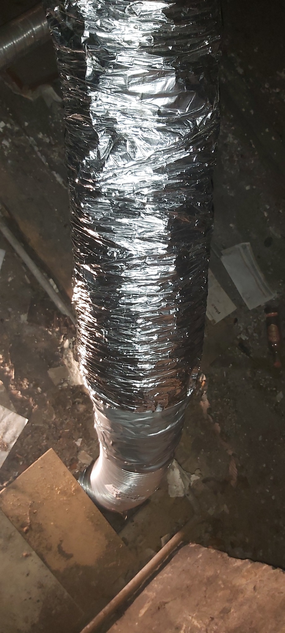 Elastyczny, aluminiowy przewód wentylacyjny, częściowo owinięty folią, w trakcie instalacji w trudno dostępnym miejscu.