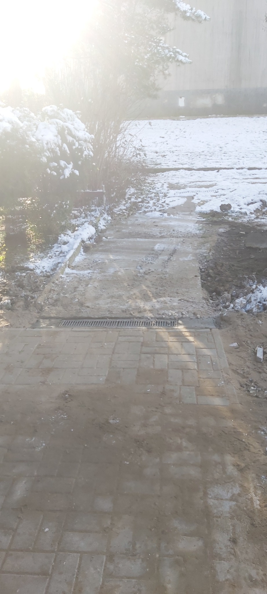 Świeżo ułożona, mokra kostka brukowa z odpływem liniowym w zimowej scenerii, częściowo pokryta śniegiem.