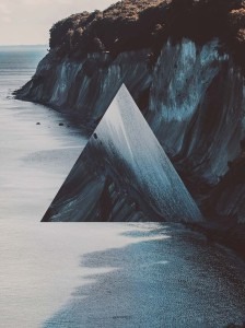 Abstrakcyjna kompozycja przedstawiająca trójkąt nałożony na krajobraz klifów nad brzegiem morza. Kolorystyka utrzymana w chłodnych odcieniach szarości i błękitu. Trójkąt ma teksturę przypominającą...