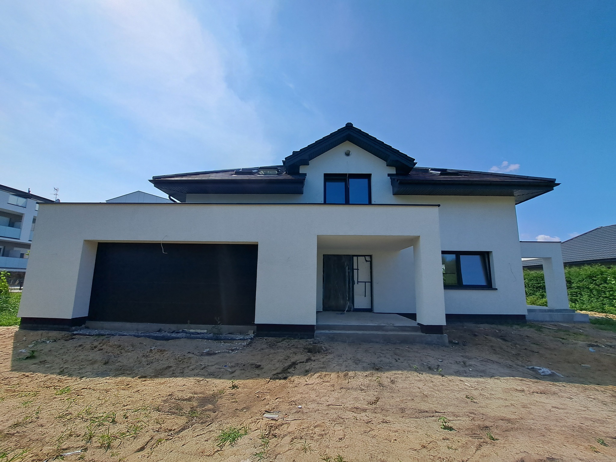 Nowoczesny dom jednorodzinny z płaskim dachem i garażem wbudowanym, jeszcze w trakcie wykończenia terenu wokół budynku.