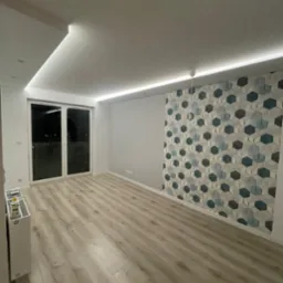 Pusty pokój po remoncie z panelami podłogowymi, ozdobną ścianą z geometrycznym wzorem tapety w odcieniach szarości i błękitu oraz oświetleniem LED w suficie.