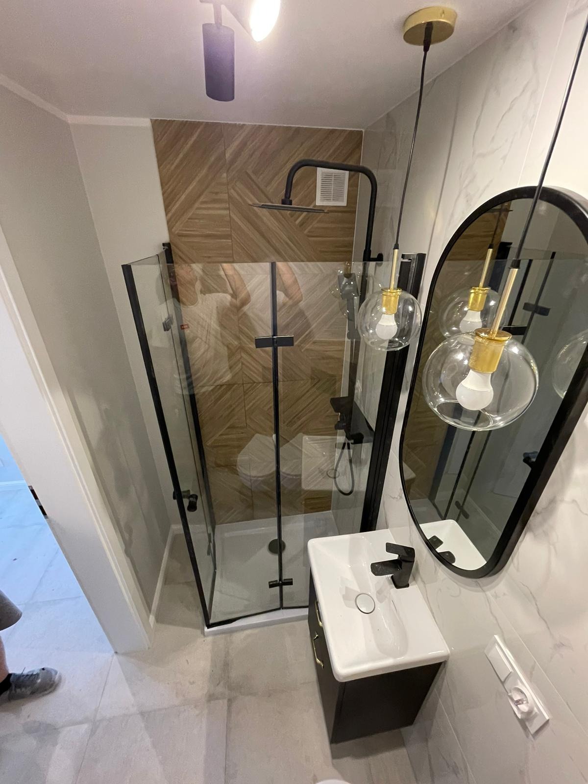 Nowoczesna łazienka po remoncie w Kaliszu z kabiną prysznicową typu walk-in z czarnymi profilami, umywalką nablatową na szafce w kolorze antracytowym i okrągłym lustrem z podświetleniem.