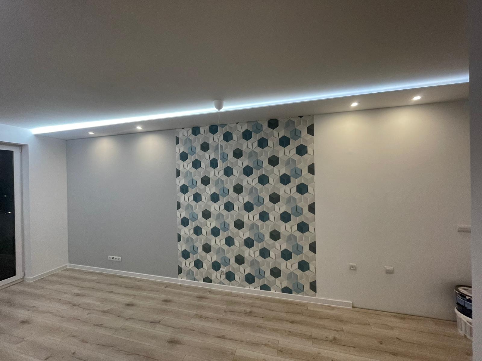 Nowoczesne wnętrze po remoncie: ściany pomalowane na szaro i biało, fragment ściany pokryty tapetą w geometryczne wzory (sześciokąty), jasna podłoga, oświetlenie sufitowe LED.