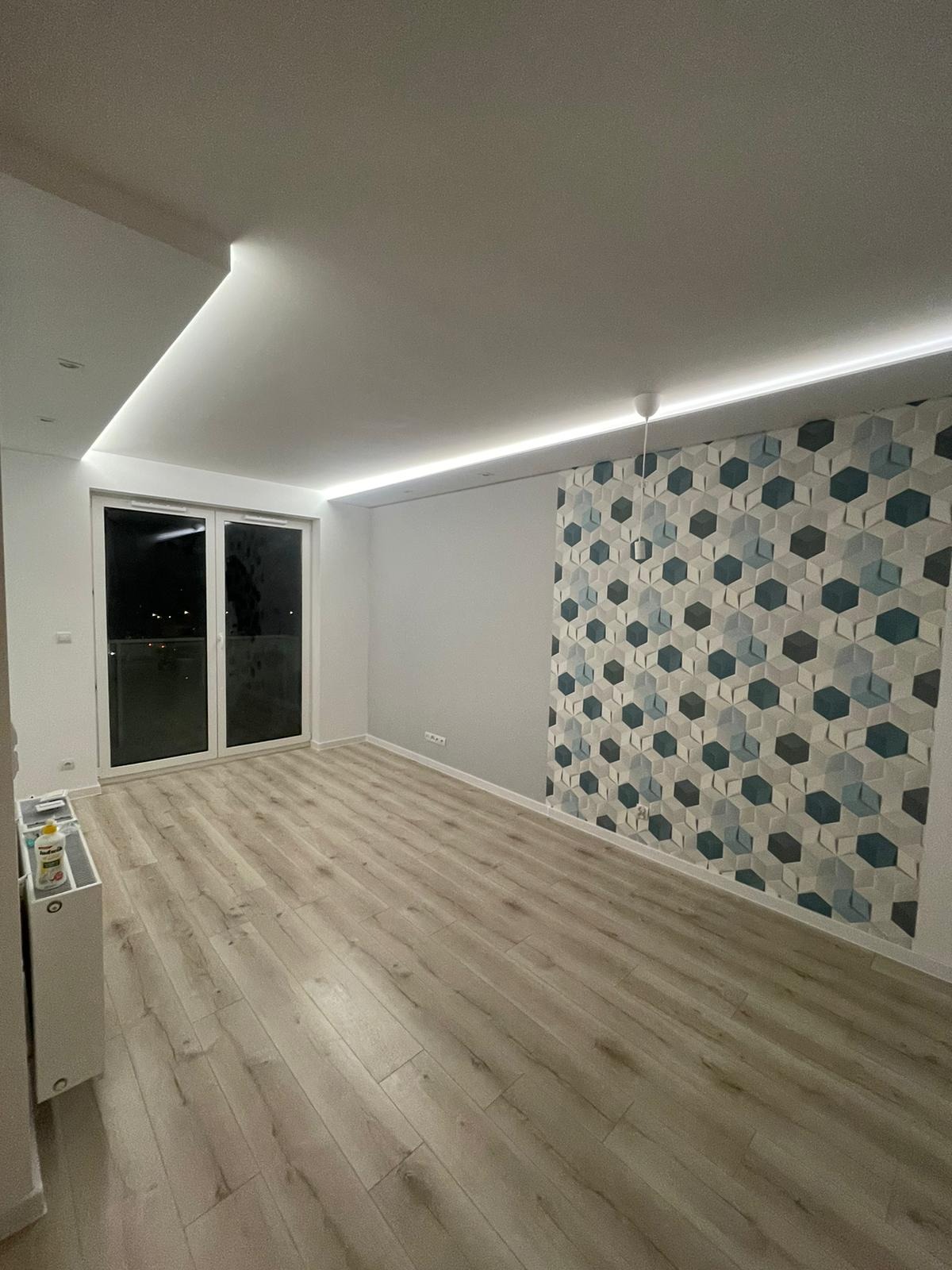 Pusty pokój po remoncie z panelami podłogowymi, ozdobną ścianą z geometrycznym wzorem tapety w odcieniach szarości i błękitu oraz oświetleniem LED w suficie.