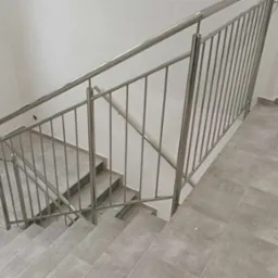 Klatka schodowa z szarymi płytkami i metalową balustradą z wypełnieniem pionowym, widok z góry schodów.