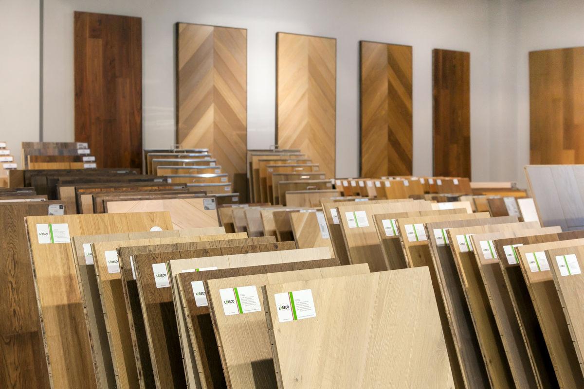 Ekspozycja różnorodnych paneli podłogowych w sklepie, z widocznymi próbkami w różnych odcieniach drewna i wzorach ułożonymi rzędami, pionowe panele z drewna na ścianie w tle.