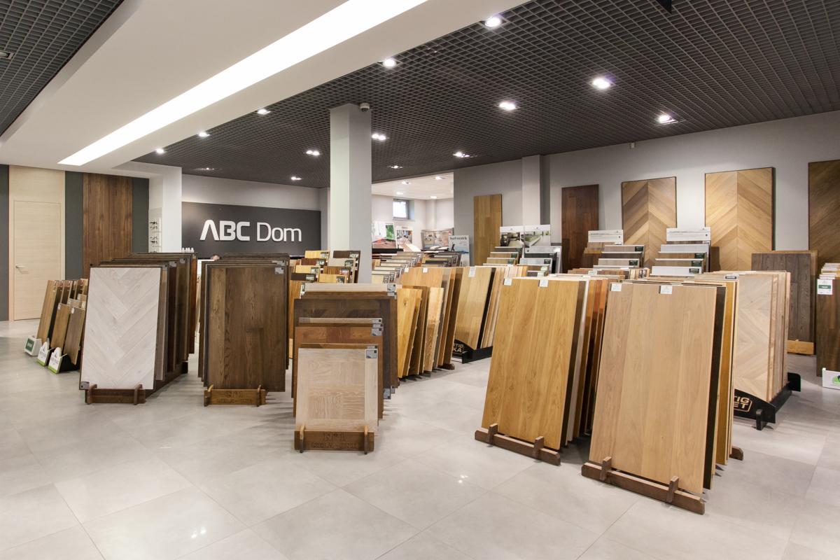 Ekspozycja różnorodnych paneli podłogowych w sklepie ABC Dom, prezentująca różne odcienie drewna i wzory ułożenia, w tym parkiet w jodełkę na ścianie w tle.