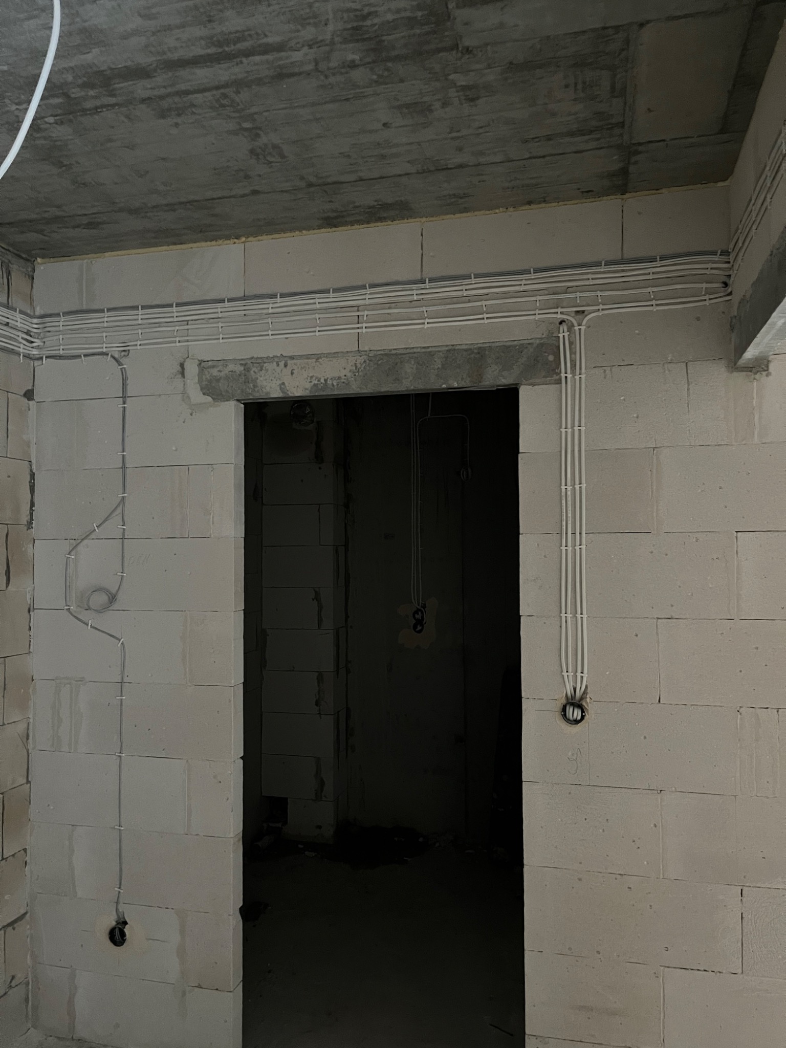 Surowy stan wnętrza z widocznymi przewodami elektrycznymi poprowadzonymi po ścianach z betonu komórkowego, widoczne puszki instalacyjne.