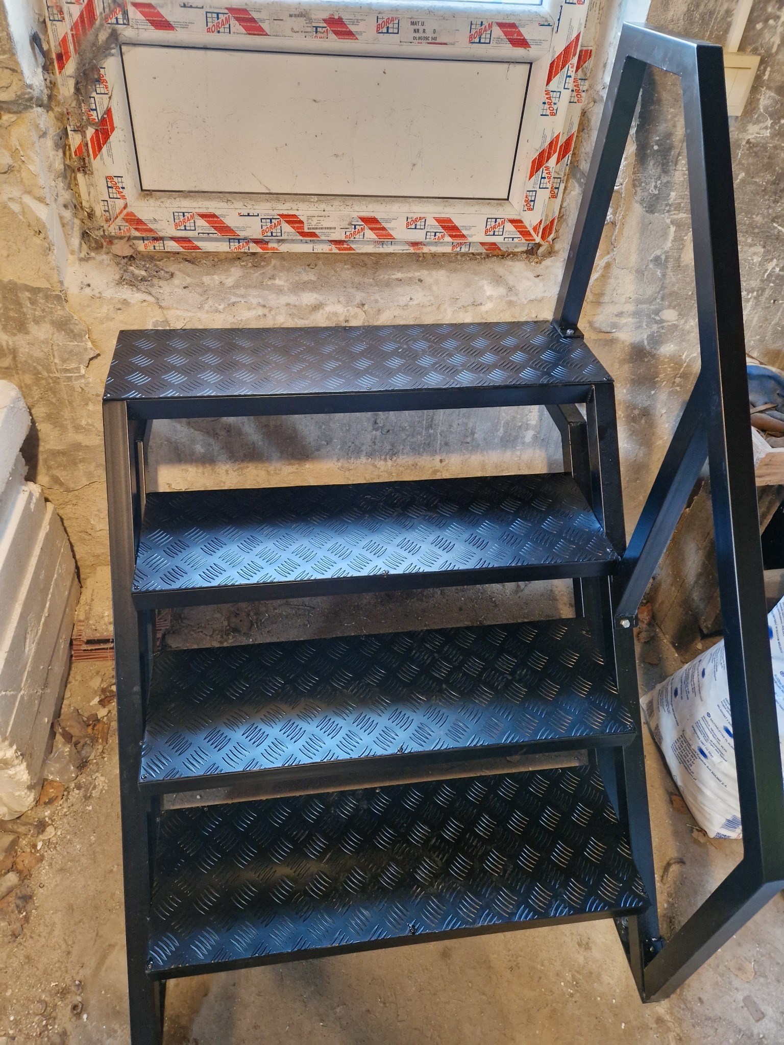 Metalowe schody z blachy ryflowanej, czarna konstrukcja, widoczne spawy, surowe wnętrze w trakcie remontu.