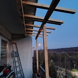 KSAL GREEN Pielęgnacja Ogrodów Kamil Kozioł - Konstrukcja drewniana zadaszenia na balkonie w trakcie montażu, widok na zewnątrz, drabina oparta o ścianę, wieczorny krajobraz z księżycem w tle.