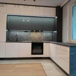 Nowoczesna kuchnia z białymi i grafitowymi szafkami, marmurowym blatem i oświetleniem LED pod szafkami wiszącymi, widok na okno.