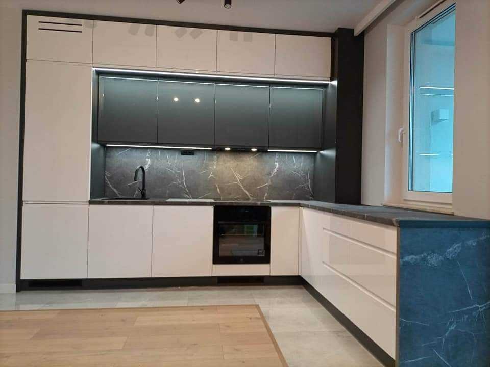 Nowoczesna kuchnia z białymi i grafitowymi szafkami, marmurowym blatem i oświetleniem LED pod szafkami wiszącymi, widok na okno.