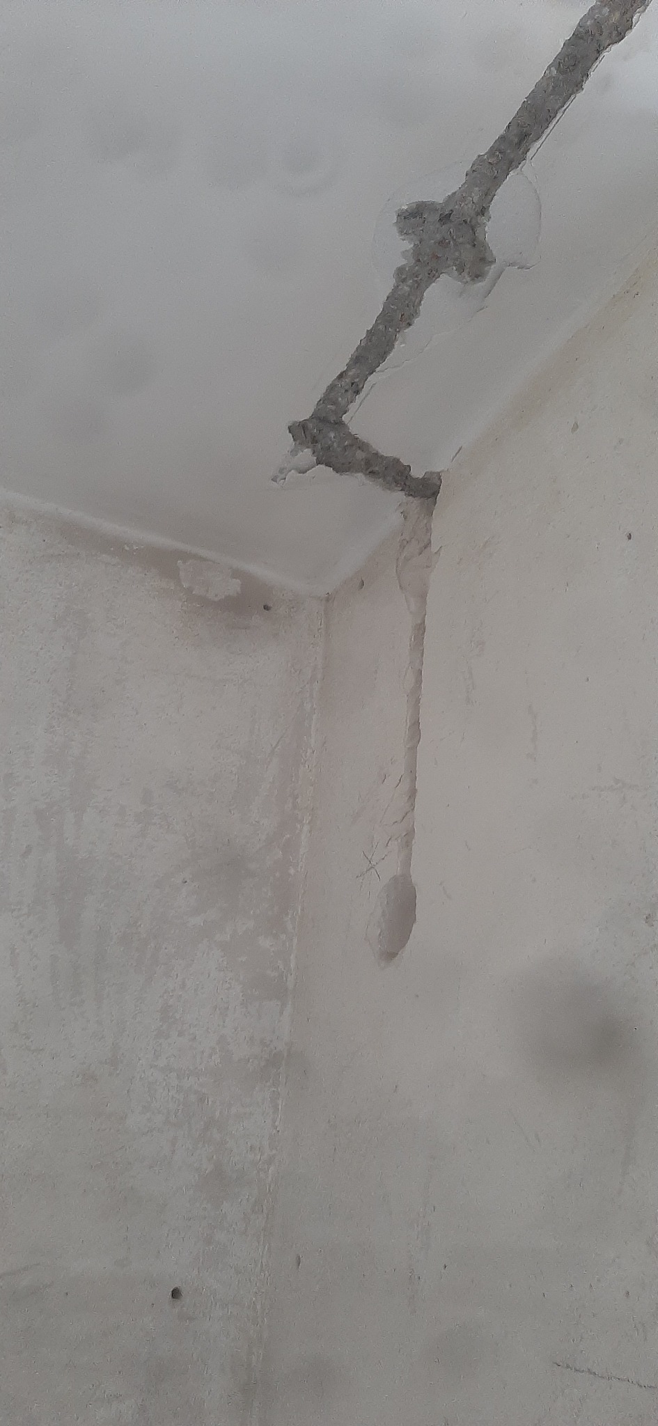 Fragment ściany i sufitu w trakcie prac remontowych, widoczne bruzdy pod kable elektryczne, ściany w stanie surowym.