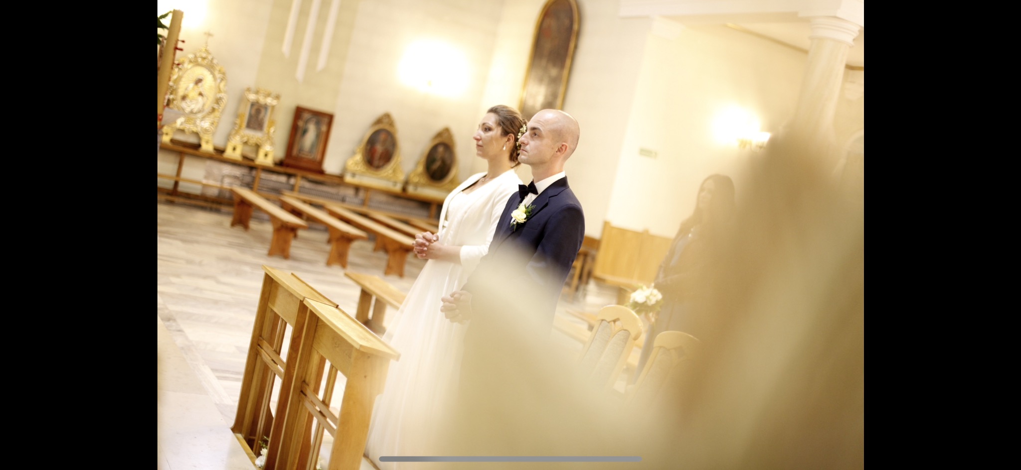 Para młoda w kościele podczas ceremonii ślubnej, widok zza ławki, oświetlenie punktowe na ołtarzu.