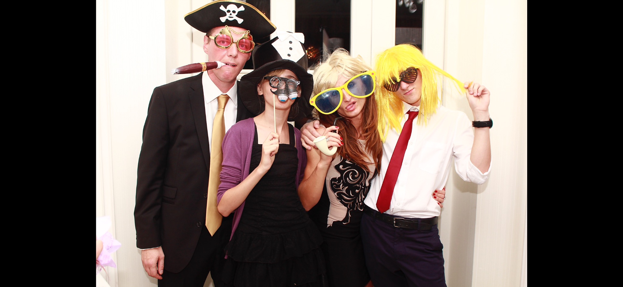Grupa czterech osób w przebraniach pozuje do zdjęcia z rekwizytami: piracki kapelusz, okulary, wąsy na patyku, peruki i cygaro.