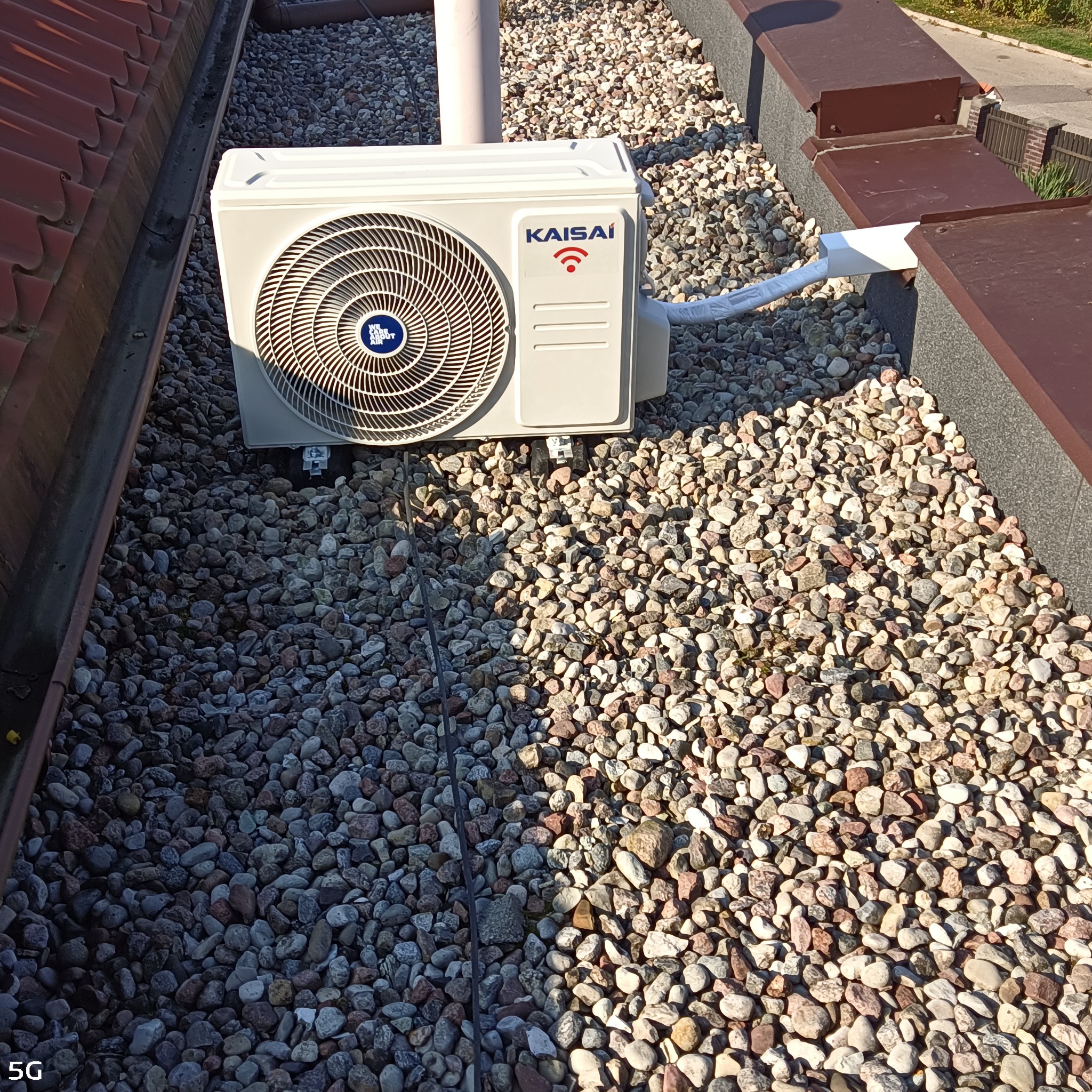 Jednostka zewnętrzna klimatyzacji Kaisai zamontowana na dachu pokrytym żwirem, widoczna rura odprowadzająca skropliny.