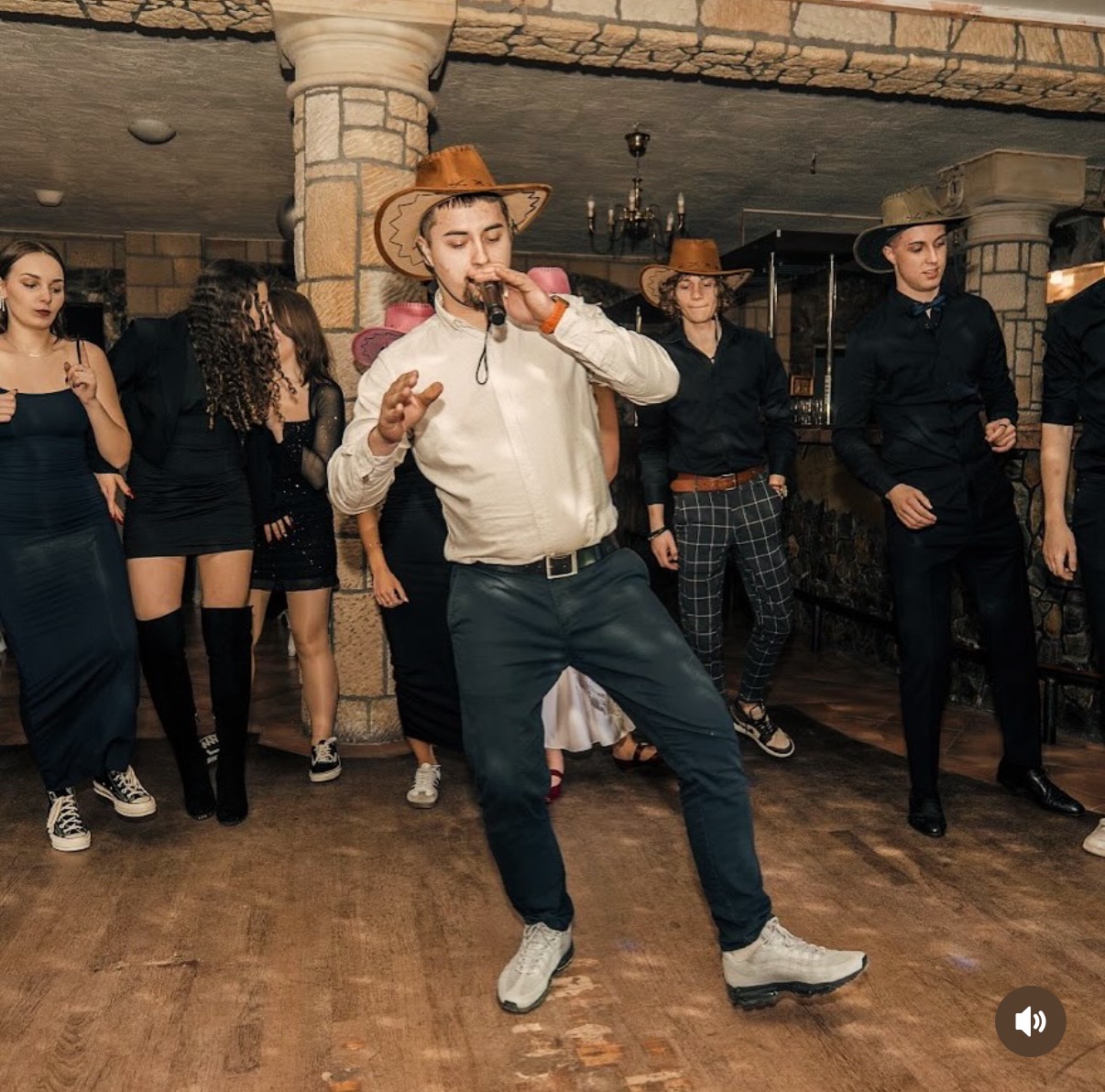 Zespół muzyczny w stylu country na scenie podczas występu. Wokalista w kowbojskim kapeluszu śpiewa do mikrofonu, a tancerki i muzycy w tle tworzą żywą atmosferę.