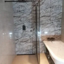 Nowoczesna łazienka z kabiną prysznicową typu walk-in z czarnymi elementami armatury i szklaną ścianką, obok biała wanna na regulowanych n&oacute;żkach, ściany wyłożone płytkami imitującymi marmur...