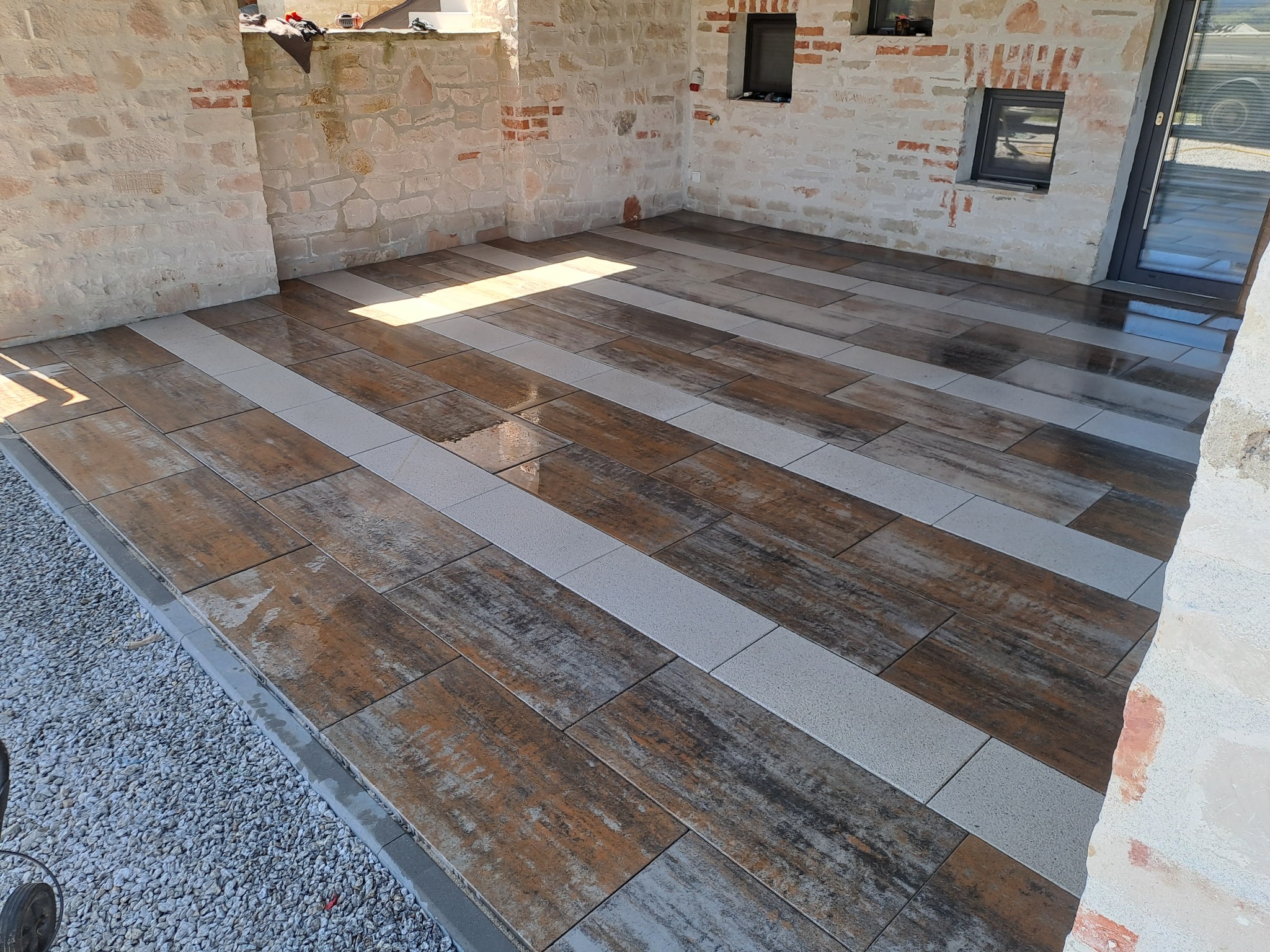 Ułożona podłoga z płytek imitujących drewno i szarych pasów w Krynicy-Zdroju. Widoczne fragmenty kamiennej ściany i okna. Efektowna aranżacja tarasu.