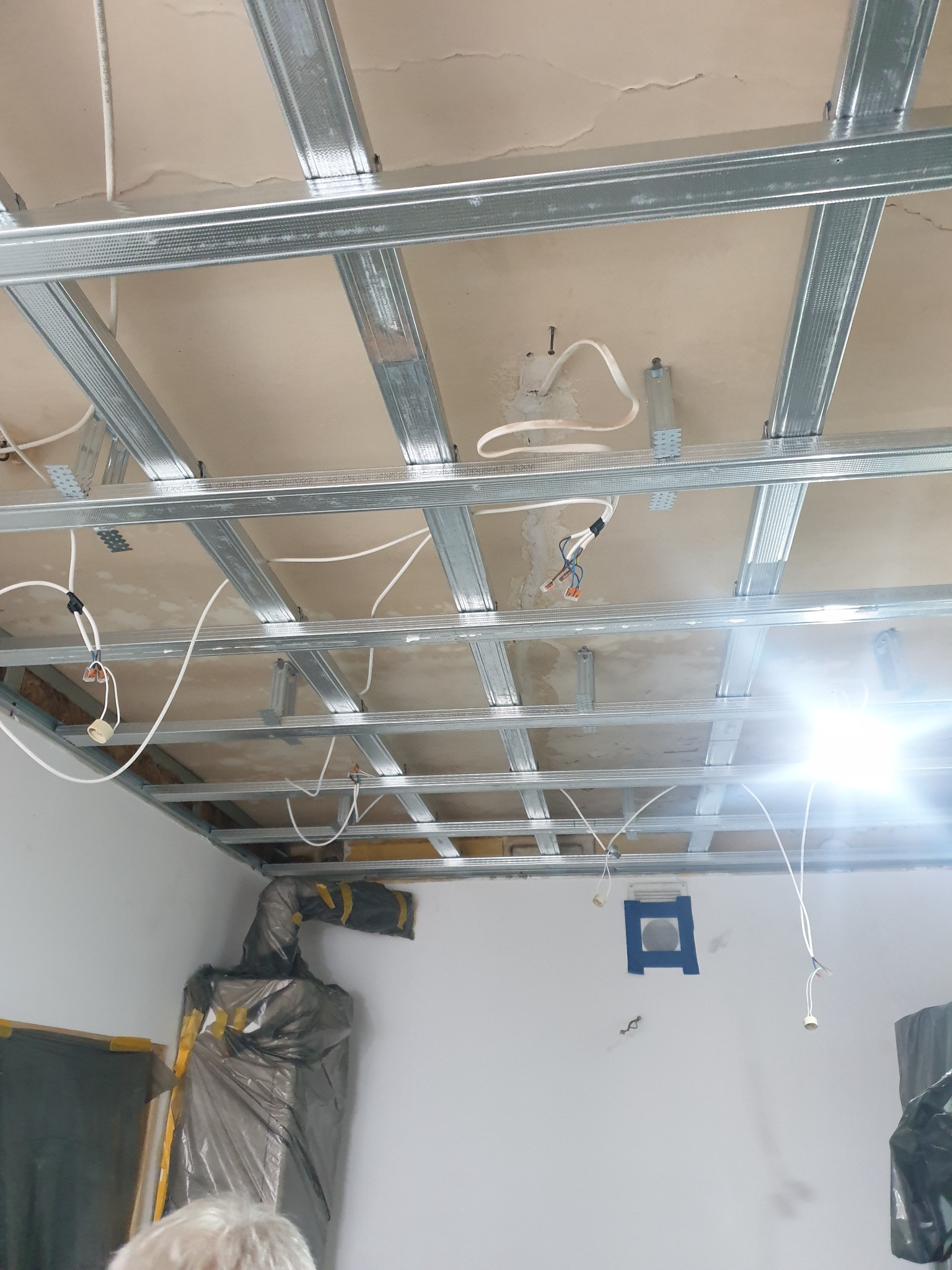Stelaż z profili metalowych podwieszanego sufitu, widoczne kable elektryczne i elementy wentylacji, przygotowanie do montażu płyt karton-gips.