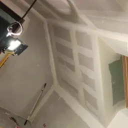 Skośny sufit poddasza z zamontowaną płytą karton gips i częściowo nałożoną gładzią, widoczna drabina malarska, lampa halogenowa i akcesoria malarskie