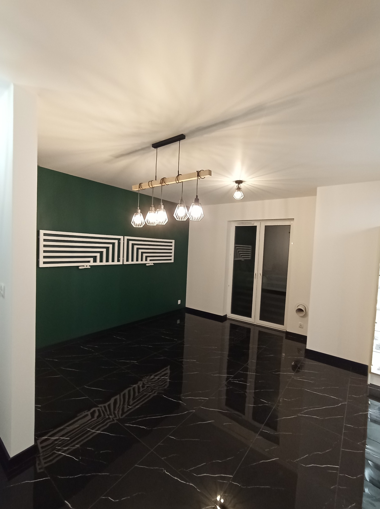 Nowoczesne wnętrze z czarną marmurową podłogą, zieloną ścianą z geometryczną dekoracją i designerskim oświetleniem wiszącym.