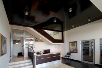 Recepcja z podwieszonym sufitem z płyt kartonowo-gipsowych, widoczne schody z drewnianą balustradą i szklane ścianki działowe.