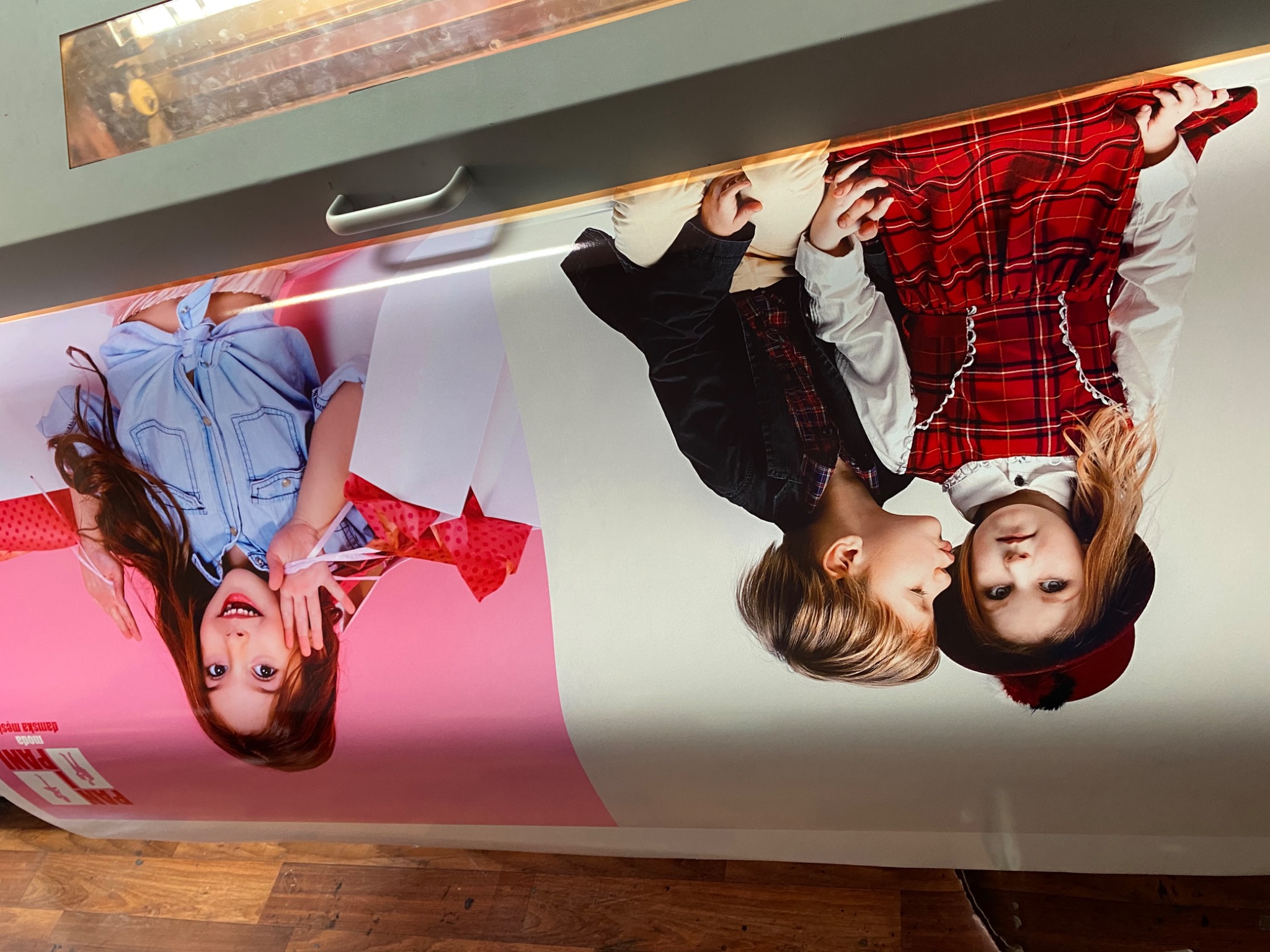 Wielkoformatowy wydruk z wizerunkiem dwójki dzieci, jedno w dżinsowej koszuli, drugie w czerwonej sukience w kratę, na drukarce przemysłowej.