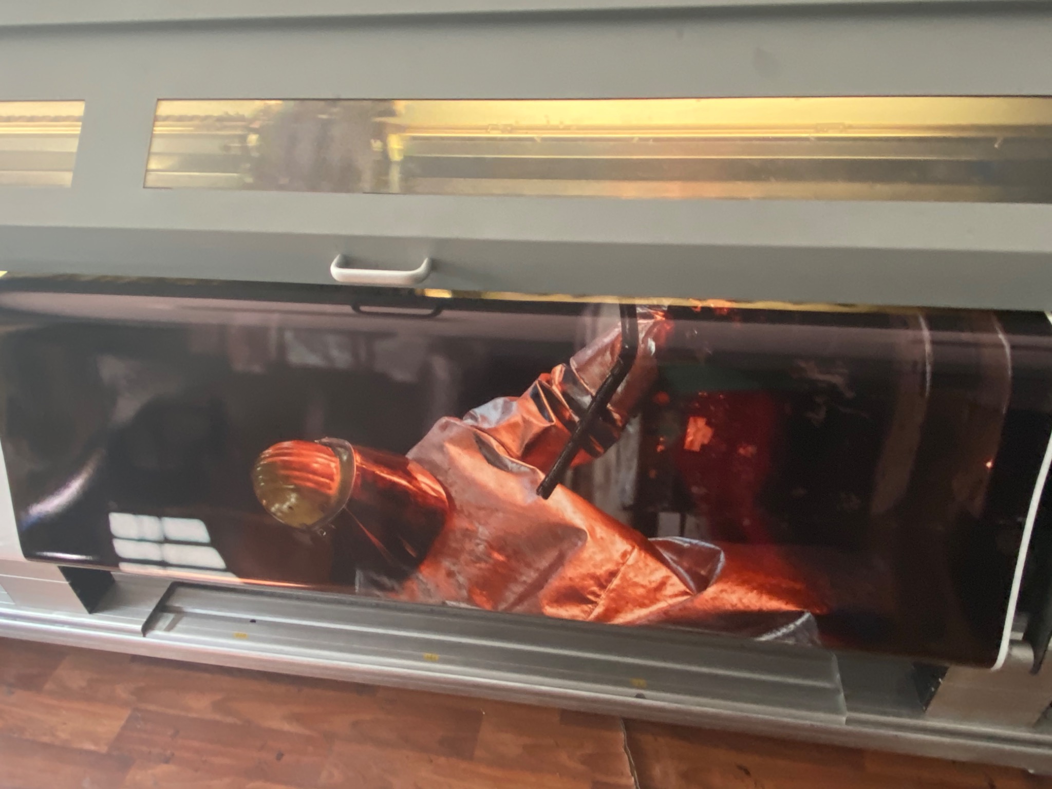 Drukarka wielkoformatowa w trakcie drukowania plakatu z motywem kosmicznym, widoczny fragment kombinezonu astronauty w odcieniach czerwieni i brązu.