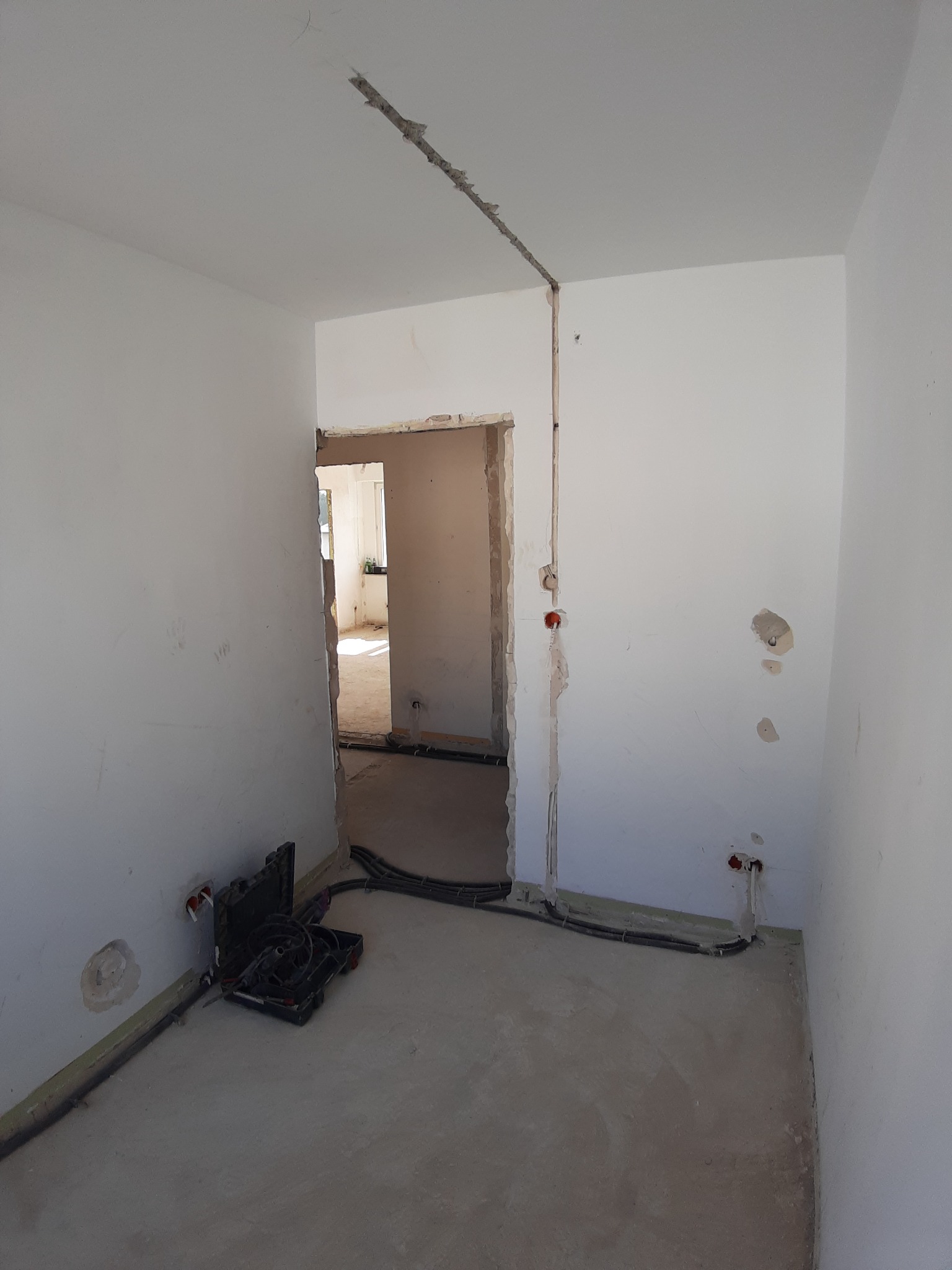 Wnętrze w trakcie remontu, widoczne kable elektryczne w ścianach i na podłodze, otwarta skrzynka narzędziowa z elektronarzędziami przy ścianie, przygotowane bruzdy pod instalację.