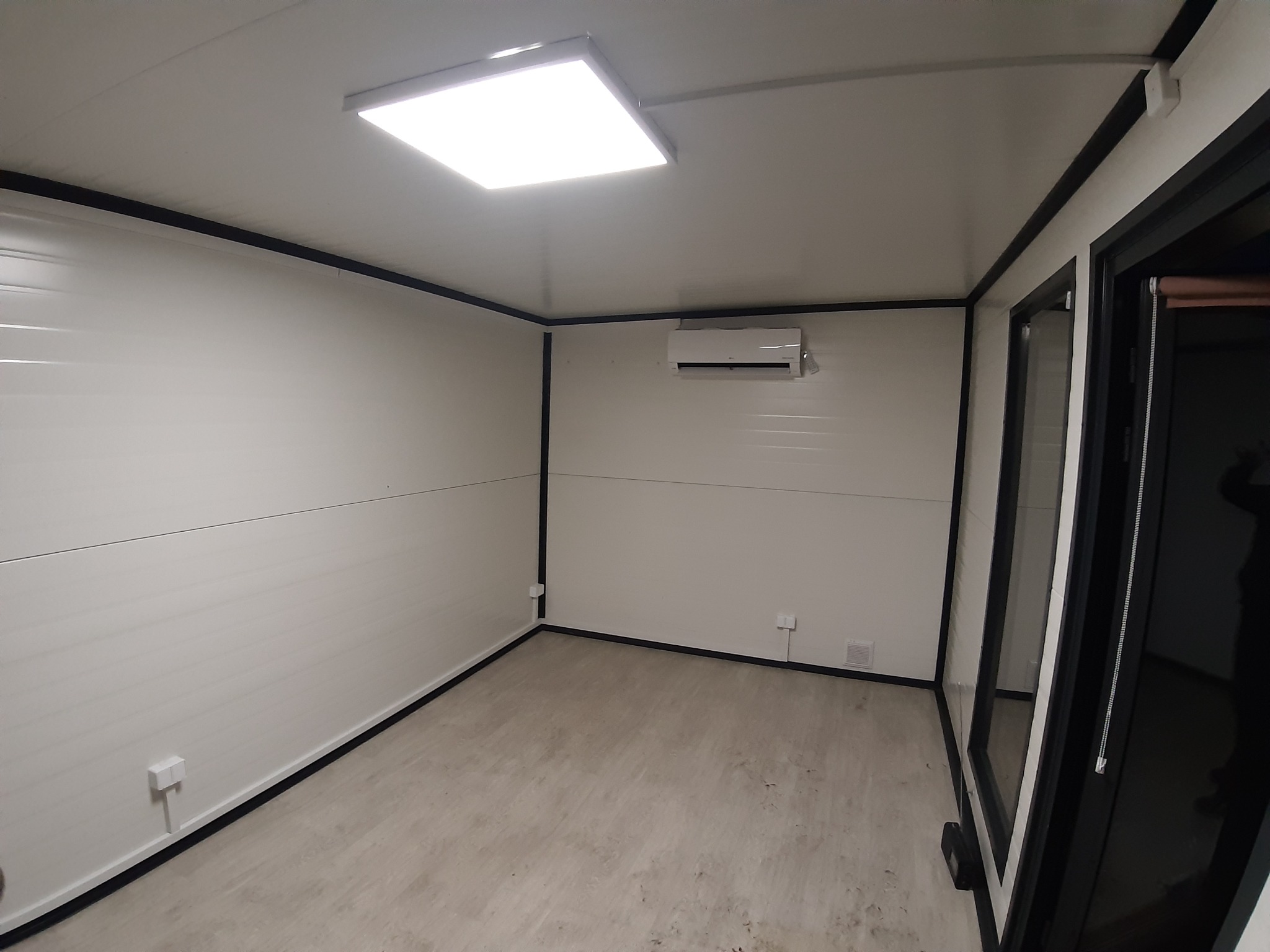 Wnętrze modułowego pomieszczenia biurowego z klimatyzacją, oświetleniem LED i gniazdkami elektrycznymi zamontowanymi na ścianach.