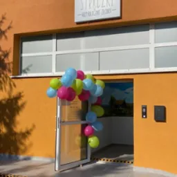 Wejście do niepublicznego żłobka 'Strączki' udekorowane balonami w kolorach niebieskim, różowym i zielonym, z widocznym logo żłobka na budynku.